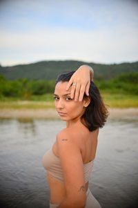 Portrait of young woman standing against lake during sunset