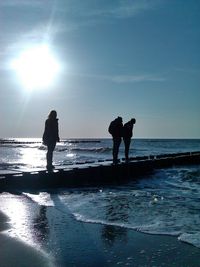 Full length of silhouette friends standing on broken pier at beach