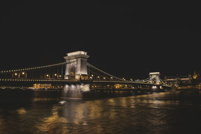 Illuminated bridge over river in city against sky at night