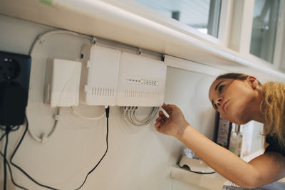 Teenage girl adjusting equipment mounted on wall at home