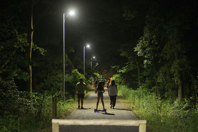 People on illuminated street amidst trees at night