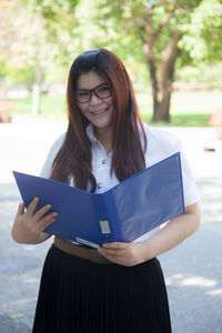 Portrait of smiling young woman with folder at park