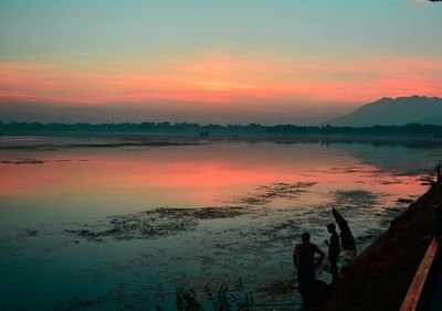Silhouette people standing by lake against sky during sunset
