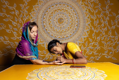 Indian artisan is applying mehndi on the hands of a white skin bride wearing a saree.