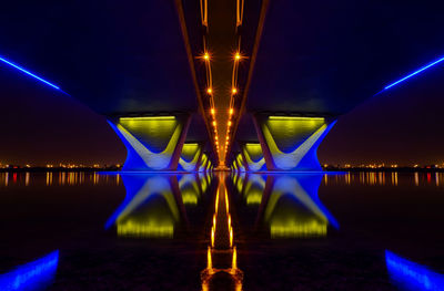 Illuminated bridge over river against sky at night