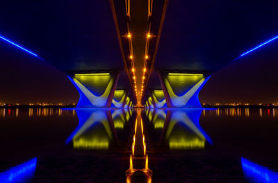 Illuminated bridge over river against sky at night