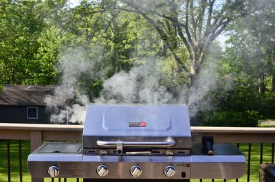 Electric barbecue grill steaming by railing against trees
