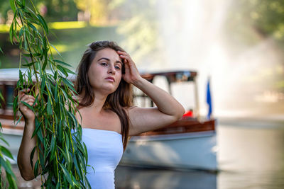 Young woman looking away while standing by water