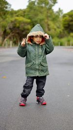 Portrait of boy gesturing peace sign while wearing hood jacket on road