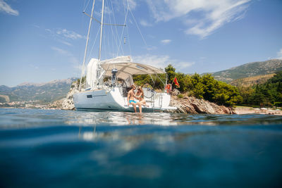 Low angle view of couple on sailboat in sea against sky