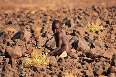 Full length portrait of naked boy sitting on rocks