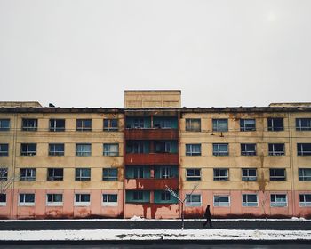 Person walking on street by building against clear sky during winter