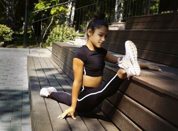 Girl in sportswear on a sunny summer day on the embankment in the park doing fitness and stretching