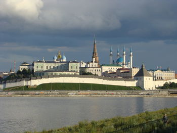 View of buildings by river against cloudy sky