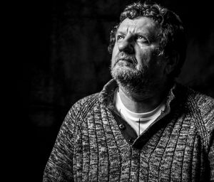 Thoughtful mature man standing against black background