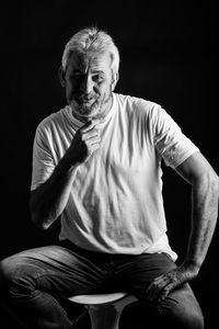 Portrait of man sitting against black background