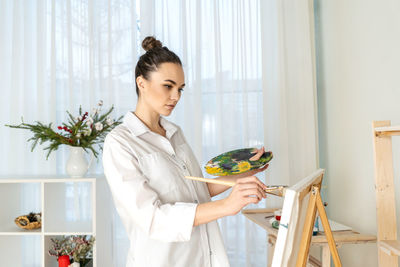 Young woman painting while standing at home