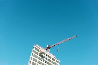 Low angle view of crane by building against clear blue sky