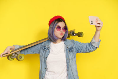 Portrait of young woman using mobile phone against yellow background