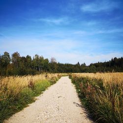 Dirt road amidst field against sky