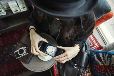 Directly above shot of young woman photographing coffee through smart phone in creative office