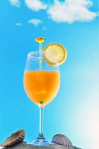 Close-up of drink on table against blue sky. orange juice cocktail on the beach sand