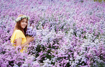 Portrait of smiling young woman against purple flowering plants