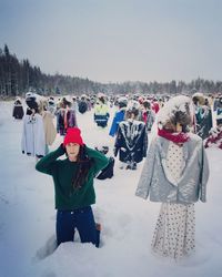 Portrait of mature woman kneeling amidst sculptures on snow covered field against sky