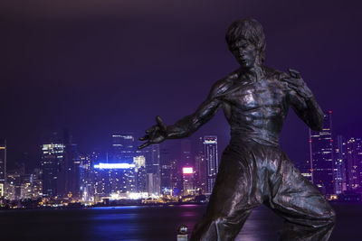 Statue by illuminated buildings against sky at night