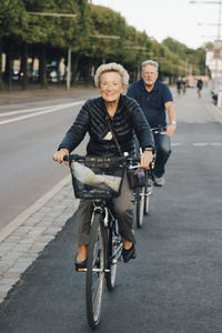 Smiling senior woman with man riding bicycles on city street