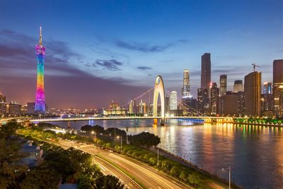 Illuminated city buildings by river against sky