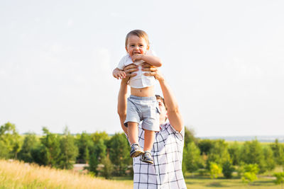 Happy boy standing on field against sky