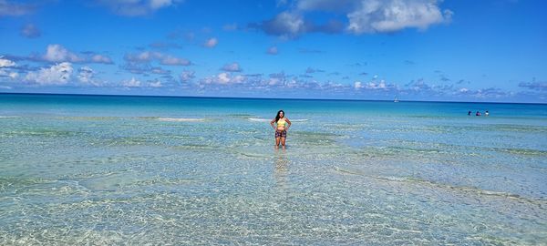 Rear view of woman standing at beach against sky