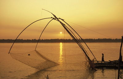 Side view of man standing on pier by arranged fishing net in sea at sunset