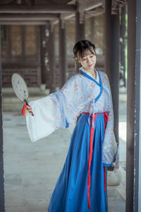 Woman in kimono holding hand fan at corridor