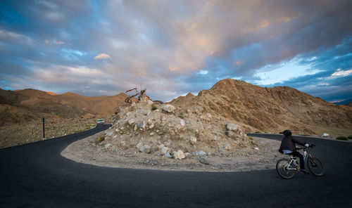 Man cycling on mountain road against cloudy sky