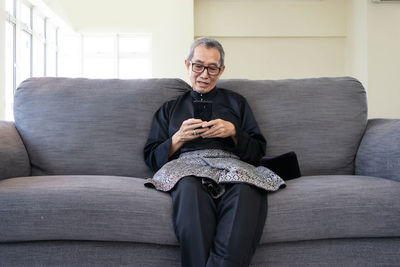 Full length of man sitting on sofa at home