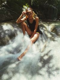 Full length portrait of woman sitting at waterfall