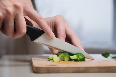 Close-up of female hands cutting on wooden cutting board fresh green cucumber for salad, home food