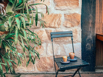 2 espresso coffees on chair against stone wall in garden setting 