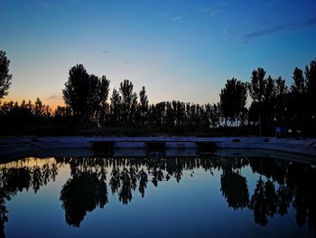 Reflection of silhouette trees in lake against sky during sunset