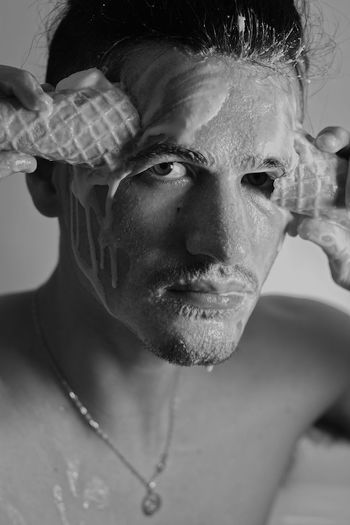 Close-up portrait of shirtless man face covering by ice cream indoors