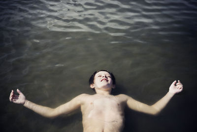 Overhead view of shirtless boy floating on sea during sunny day