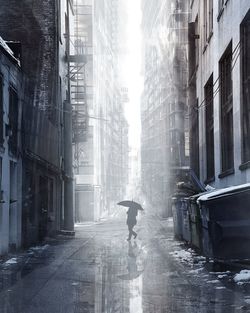 Man with umbrella walking on street amidst buildings in city during rainy season