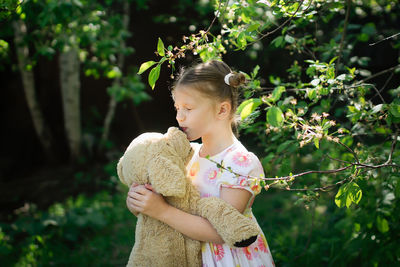 Cute european kid girl in dress with soft big toy dog in backyard, in park summer