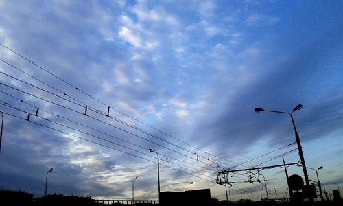 Low angle view of electricity pylon against cloudy sky