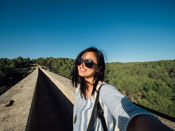 Portrait of young woman wearing sunglasses standing against blue sky