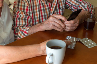 Midsection of man holding coffee cup on table