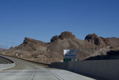 Road leading towards mountains against clear blue sky