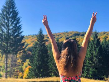 Rear view of woman with arms raised standing on field against clear blue sky